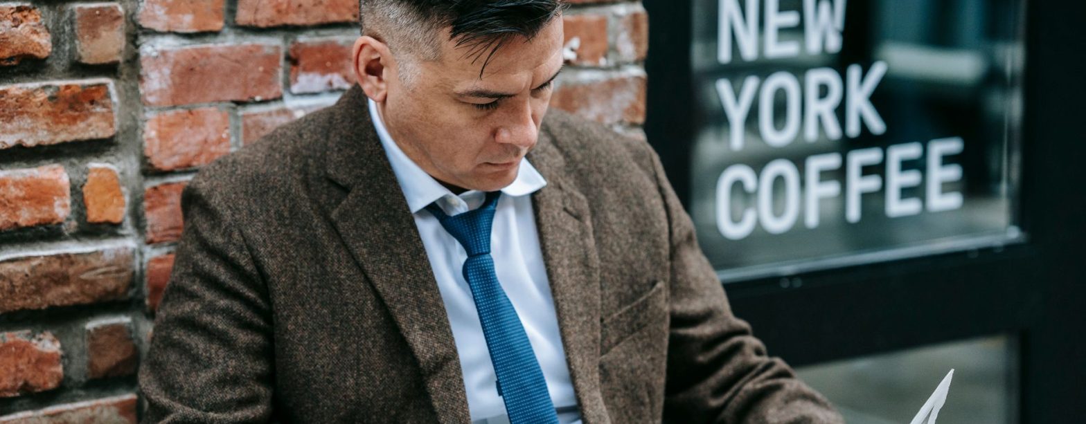 Man in formal attire reading a newspaper outside New York coffee shop. — Nangs Sydney | Professional Nangs Delivery Across Sy